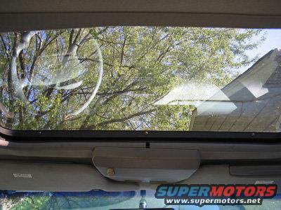 Interior view of a car's sunroof with trees and a house roof visible through the glass