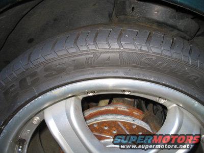 Close-up of a car's front tire and slotted brake rotor. The tire has 'ESTA' and 'Supra' visible
