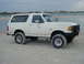 1989 Ford Bronco - White 1989 Ford Bronco sits on a sandy beach near the water with people in the distance.
