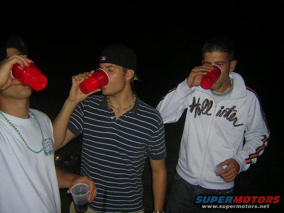 Three men drinking from red cups at night