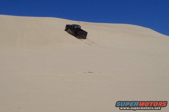 Black pickup truck driving down a sand dune under a clear blue sky