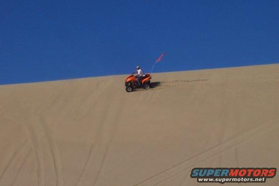 Orange ATV with rider on a sand dune under a blue sky