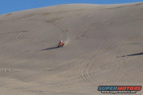 Orange ATV with rider on sand dune, leaving tire tracks