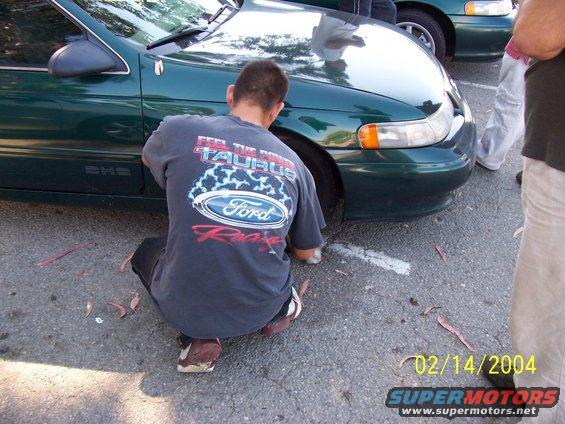 Green sedan front view, person crouching by wheel. Date stamp 02/14/2004