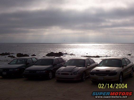 Four sedans parked on a sandy beach with the ocean and cloudy sky in the background. Date stamp reads 02/14/2004