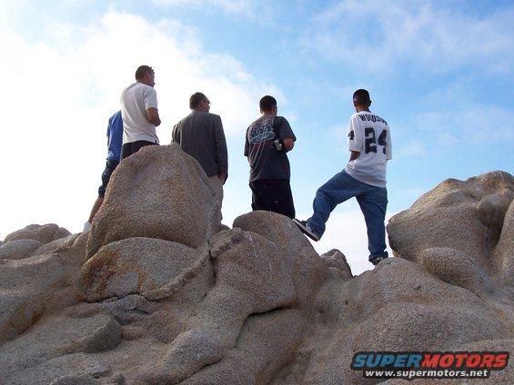 Four men stand on large rocks under a blue sky with clouds