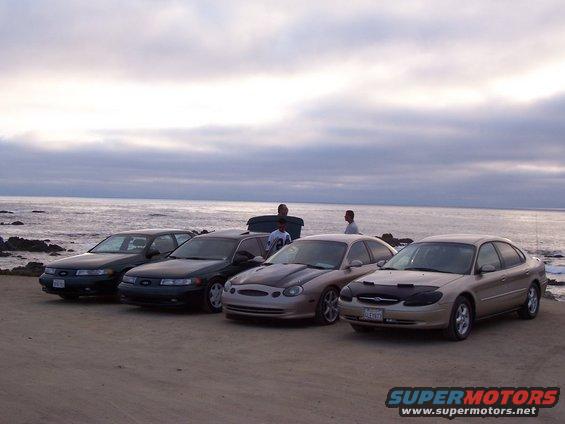 Four 1998 Mercury Sables parked on a beach with the ocean in the background