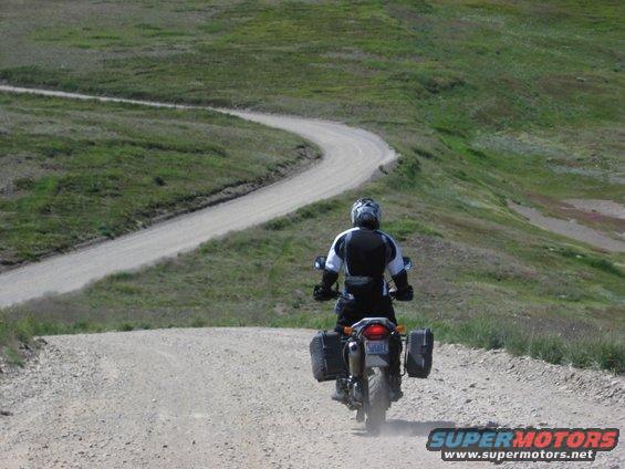 Motorcyclist rides up a winding dirt road through grassy hills