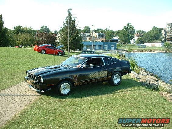 Black 1978 Ford Mustang II parked by water, red Mustang in background