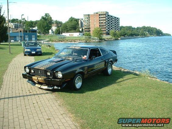 Black 1978 Ford Mustang II coupe with gold stripes parked by water