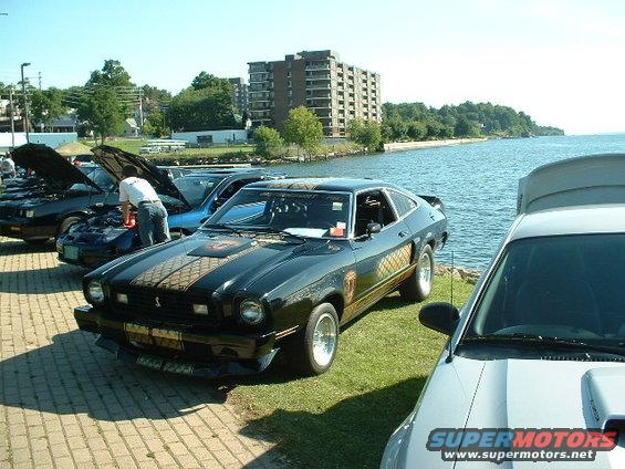 Black 1978 Ford Mustang II with gold stripe detail parked by water