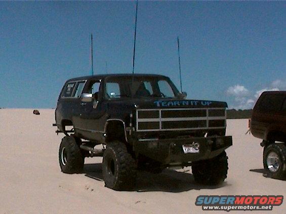 Lifted black SUV with off-road tires and 'TEAR'N IT UP' on grille. Another SUV is partially visible to the right