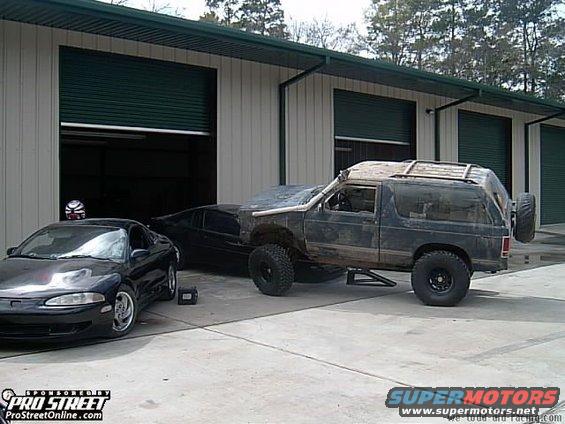 Dark off-road SUV with lifted suspension and spare tire on rear, parked outside garage