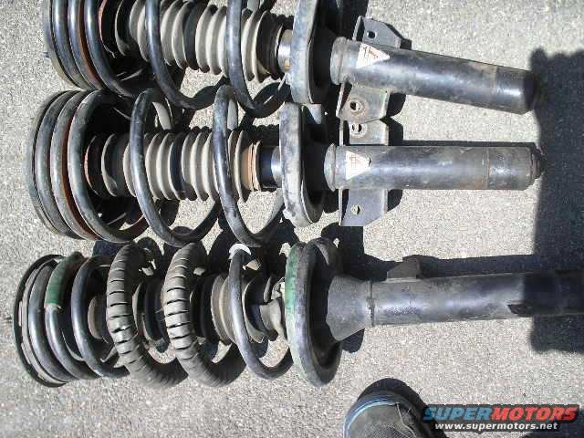 Three car suspension struts with coiled springs, some with green and tan accents, lying on a gray surface