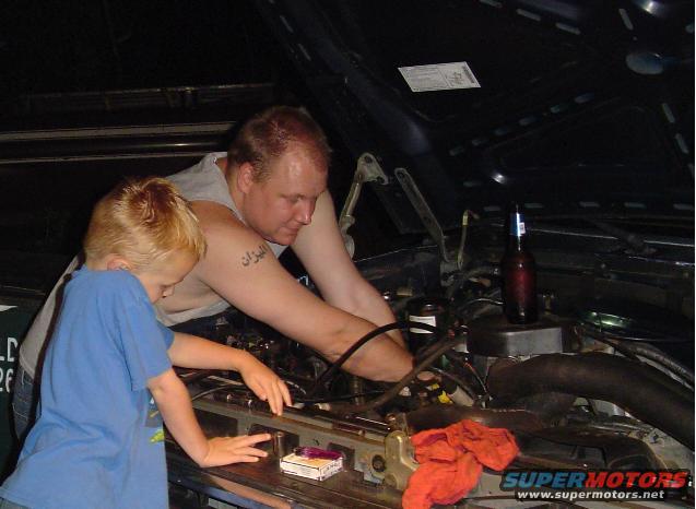 guy and kid looking at car engine, beer bottle nearby