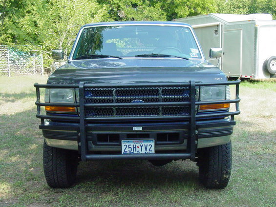 Front view of a dark blue Ford F-Series truck with a large black brush guard and a trailer behind it