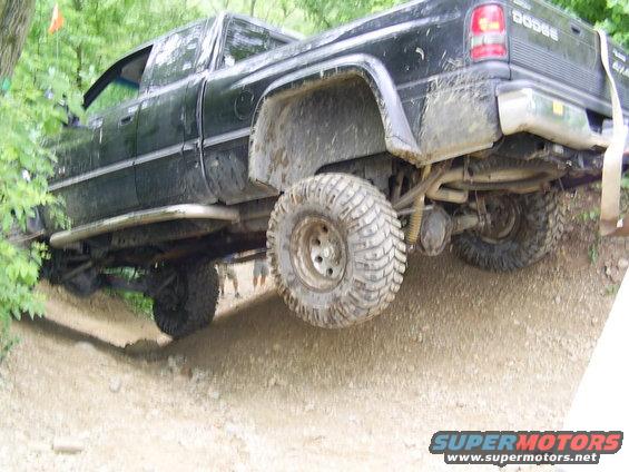 Black Dodge pickup truck with large off-road tires climbing a dirt hill