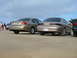 1995 Ford Taurus - Two sedans are parked on a dirt lot under a cloudy sky, with people visible in the background.