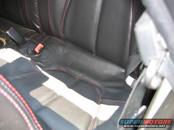Black leather car seats with red stitching, seatbelts, and a watermark