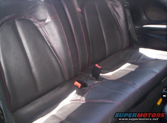 Back seat of a car with black leather seats and red stitching. Seatbelts are visible
