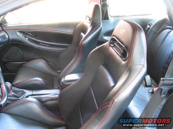 Car interior showing black leather racing seats with red stitching, and part of the center console
