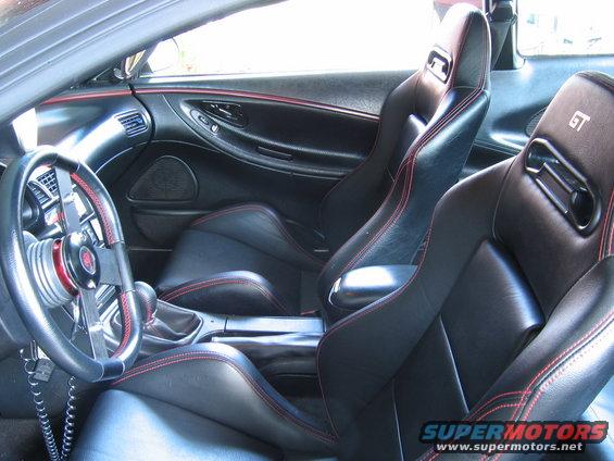Car interior with black leather seats with red stitching, aftermarket steering wheel, and GT badging on headrests