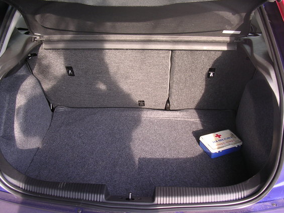 Car trunk interior showing grey carpet and a blue and white first aid kit