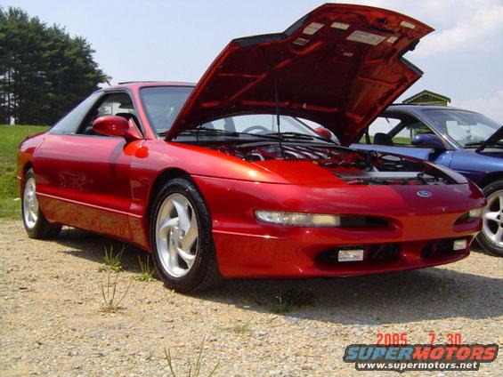 Red 1995 Ford Probe coupe with hood open, parked on gravel. Front 3/4 view