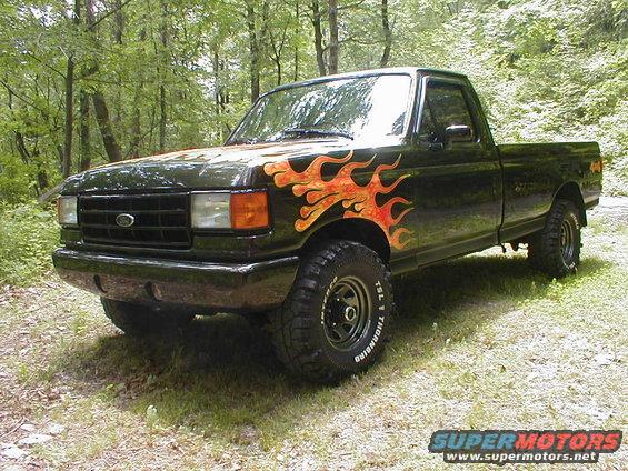 Black 1991 Ford F-150 pickup truck with flame decals on the hood and front fenders, lifted suspension, and off-road tires