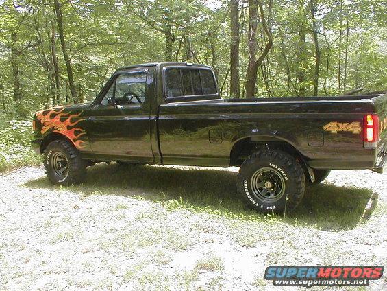 Side view of a black 1991 Ford F-150 pickup truck with flame decals and 4x4 badging
