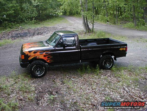 1991 Ford F-150 pickup truck with flame decals on the hood and fender, lifted with off-road tires