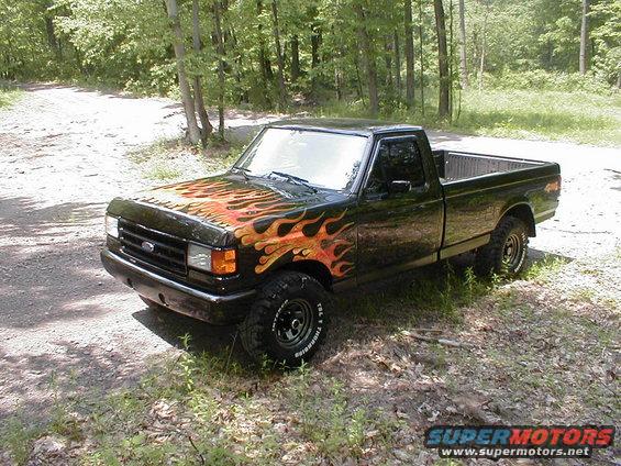 Black 1991 Ford F-150 with flame decals parked on a dirt road