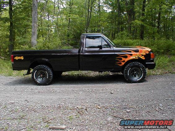 Black Ford F-150 pickup with flame decals on the hood and fender, parked on a gravel road