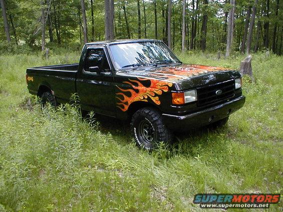 Black Ford F-150 pickup truck with flame decals on hood and fender, parked in grassy woods