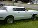 1978 Ford Mustang II - A white coupe with custom wheels and star decals sits on grass, with other vehicles visible on a road in the background.
