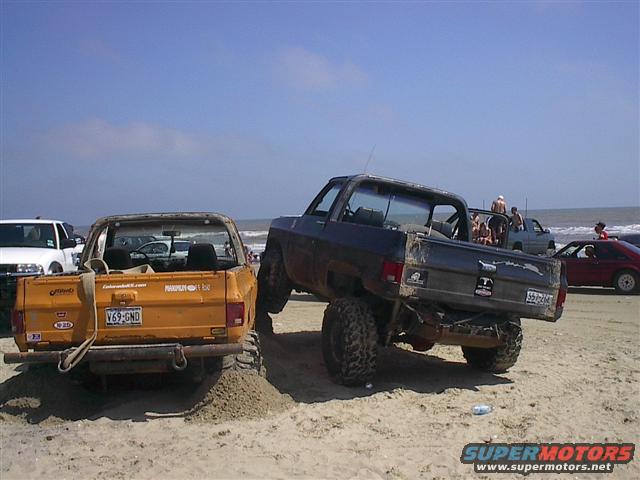 Rear view of orange pickup truck and dark SUV on sandy beach