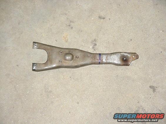 Metal clutch fork with a U-shaped end and a single mounting hole at the other end, resting on a concrete surface
