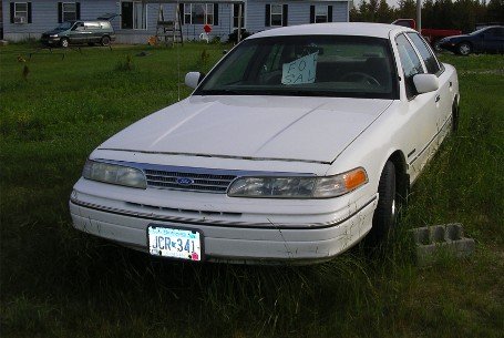 White 1998 Ford Crown Victoria sedan with a "FOR SALE" sign in the windshield, parked on grass