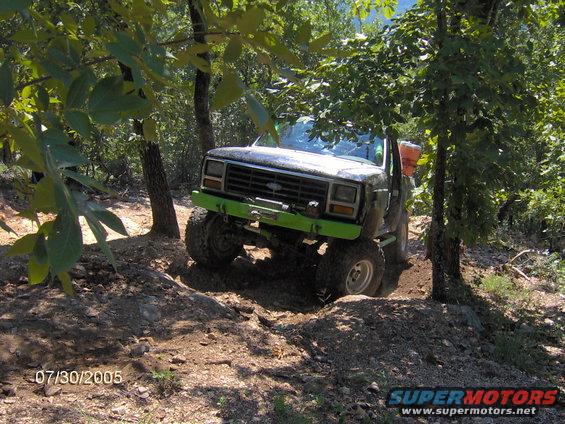 Modified pickup truck with green bumper and winch navigating a dirt trail