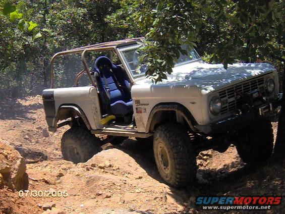 White 1978 Ford Bronco with roll cage and racing seat navigating a dirt trail