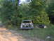 1978 Ford Bronco - An abandoned vehicle sits in a wooded area, stripped of its components and surrounded by debris.