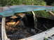 1978 Ford Bronco - The interior of a derelict vehicle, filled with leaves and debris, is seen from the side with the doors open.