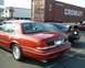 1999 Ford Crown Victoria - Rear view of a red 1999 Ford Crown Victoria, parked in a lot with other vehicles and a shipping container.