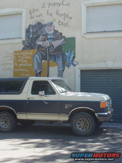 Two-tone dark blue and cream Ford Bronco parked in front of a building with a mural