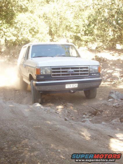 White 1987 Ford Bronco driving off-road, kicking up dust
