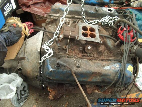V8 engine block with carburetor, distributor, and spark plug wires. Chain attached for lifting
