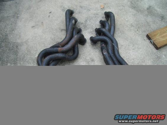 Two sets of black exhaust headers on a concrete surface
