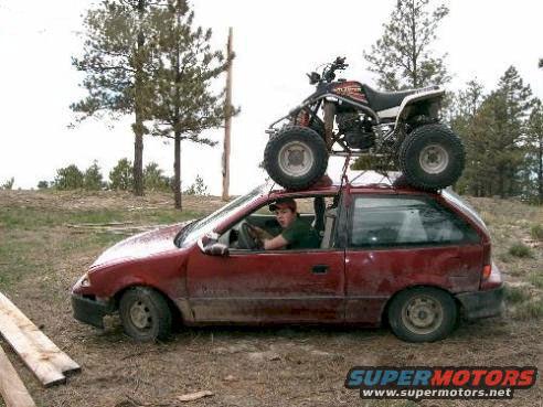 Red hatchback with an ATV strapped to its roof, driver visible inside