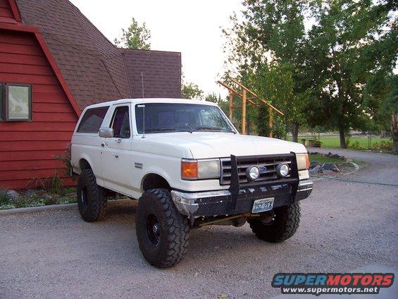 1990 Ford Bronco lifted with large tires and front bull bar parked in gravel driveway