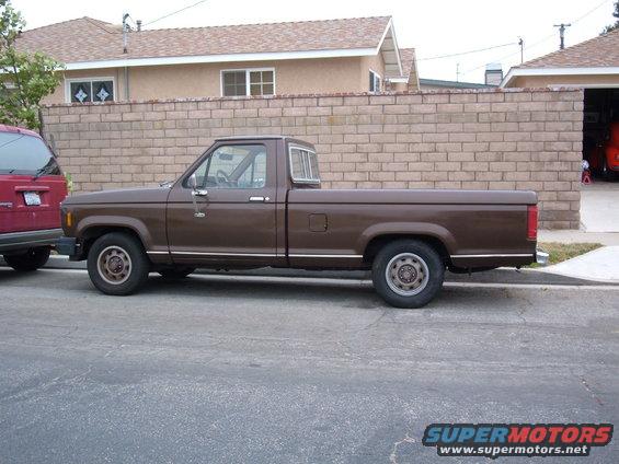 Side view of a brown 1985 Ford Ranger pickup truck parked next to a red SUV